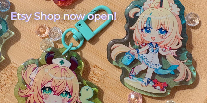 A cropped photograph of two colorful acrylic keychains featuring chibi drawings. There's a text on the top left of the image saying "Etsy Shop now open!"